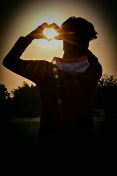 a person making a heart shape with their hands in the sun's rays behind them