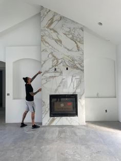 a man standing next to a fireplace in a living room with white walls and floors