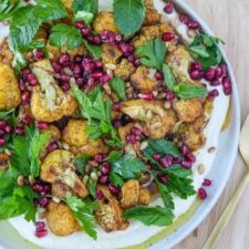 a white plate topped with cauliflower and pomegranate covered in greens