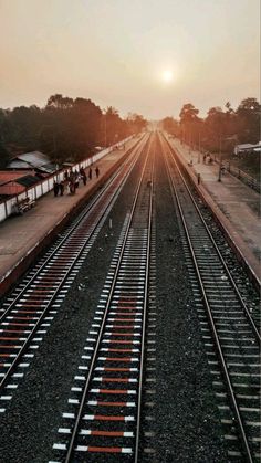 the sun is setting over train tracks in an empty area with people walking on one side