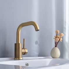 a gold faucet sitting on top of a white sink next to a vase with flowers