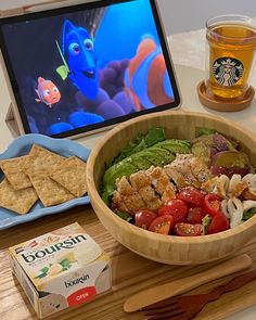 a wooden tray topped with a bowl of salad next to a laptop and tablet computer