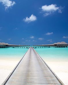 a wooden walkway leading to the beach and over water huts