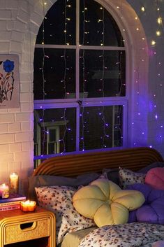 a bed with pillows and blankets in front of a window filled with purple light bulbs