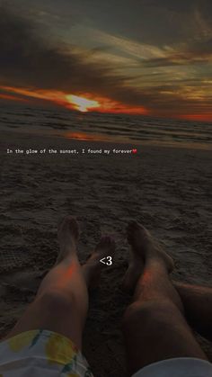 two people are laying on the beach with their feet in the sand and one person is looking out at the ocean