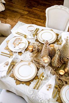 a table set for christmas with gold and white plates, silverware and napkins