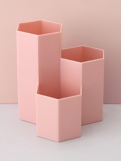 three pink vases sitting next to each other on a white counter top in front of a pink wall