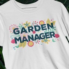 a white t - shirt with the words garden manager printed on it, sitting in front of green leaves