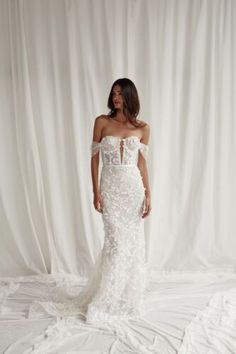 a woman in a white wedding dress standing on a white sheeted floor with her arms behind her back