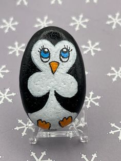 a penguin painted on top of a rock with snowflakes in the back ground