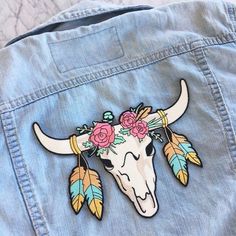 a bull skull with flowers and feathers on it's head is shown in the back pocket of a jean jacket