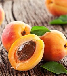 three peaches with leaves and one sliced in half on a wooden surface, ready to be eaten