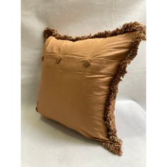 a brown pillow with fringe trim and buttons on the front, sitting on a white background