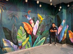 a man standing in front of a colorful wall mural with birds and tropical leaves on it