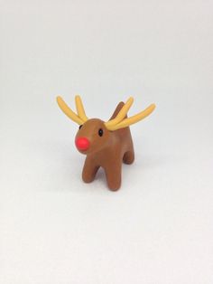 a small toy reindeer with red nose and antlers on it's head, standing in front of a white background