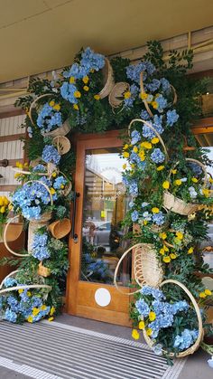 blue and yellow flowers decorate the front door of a building with wicker baskets on it