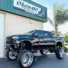 a black pickup truck parked in front of a building with large tires on it's rims