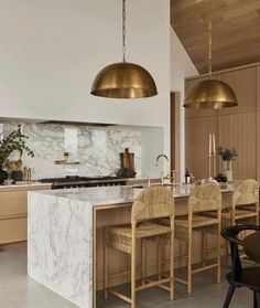 a large kitchen with marble counter tops and gold pendant lights hanging from the ceiling over the island