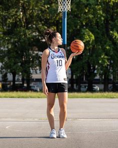 a woman holding a basketball in her right hand while standing next to a basket ball