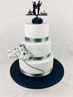 a three tiered white wedding cake decorated with black silhouettes and blue flowers on top