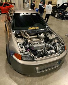 the engine compartment of a car in a showroom with people looking at cars behind it