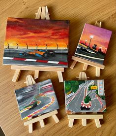 four small paintings on easels sitting on top of a wooden table next to each other