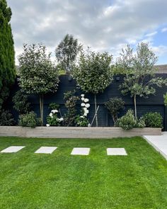 a garden with grass and trees in front of a black fenced in area that has white stepping stones on it