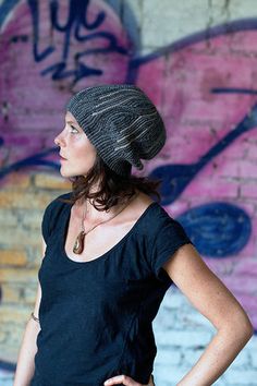 a woman standing in front of a graffiti covered wall wearing a black shirt and hat