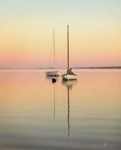 two sailboats floating in the water at sunset