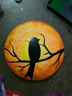 a painted rock with a bird sitting on a tree branch in front of the sun