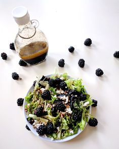 a white plate topped with a salad covered in blackberries next to a bottle of syrup