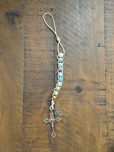 a cross is hanging from a string on a wooden surface with beads and chains attached to it