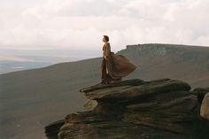 a woman standing on top of a large rock