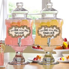 two large glass jars filled with liquid sitting on top of a table next to plates of fruit