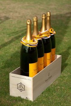 four bottles of champagne in a wooden box on the grass with a fireman's cap