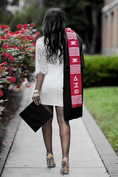 a woman walking down a sidewalk carrying a black purse and a red scarf over her head