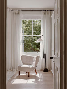 a white chair sitting in front of a window next to a lamp and a floor lamp