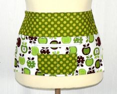 a green and white apron on a mannequin torso with an apple print design