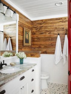 a bathroom with wood paneling and white fixtures, including a red door that leads to the toilet