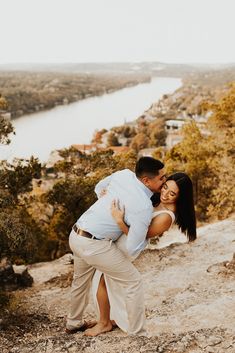 a man and woman hugging on top of a hill overlooking a river in the distance