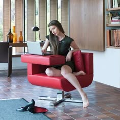 a woman sitting on a red chair using a laptop