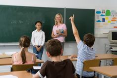 a group of children standing in front of a blackboard with their hands up to the teacher