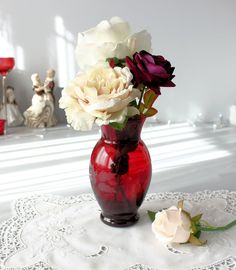 a red vase filled with white and purple flowers on top of a lace doily