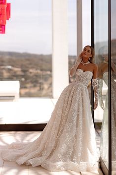 a woman standing in front of a window wearing a wedding dress