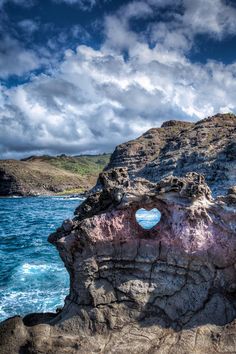 a rock formation with a hole in the middle of it on top of blue water