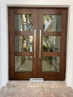 two double doors with glass panels and brick walkway in front of a white wall, surrounded by palm trees