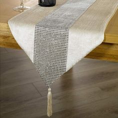 a white table runner with tassels and beads on the edge is sitting on a wooden table