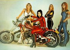 three women standing next to a motorcycle in front of a white wall with an advertisement on it