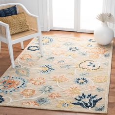 a white chair sitting on top of a wooden floor next to a rug covered in flowers