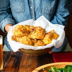 a person holding a bowl full of fried food and a glass of beer in front of them